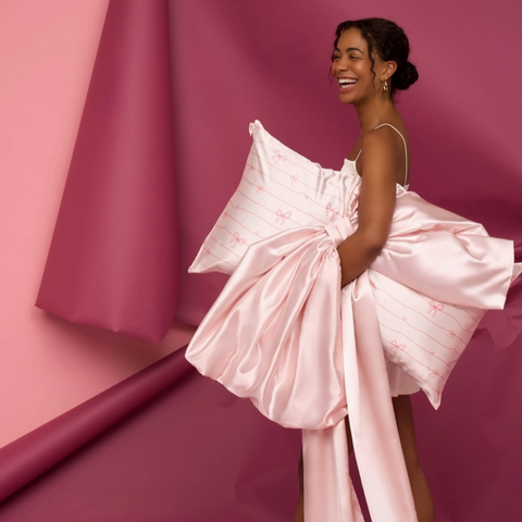 Woman in a pink dress with a large bow against a pink background