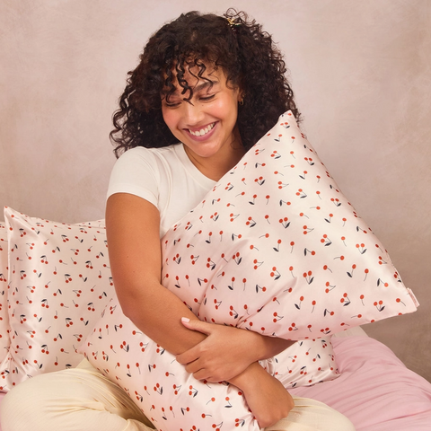 Woman holding a patterned pillow against a neutral background