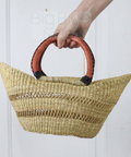 Woven handbag with red handles held by a person against a white background