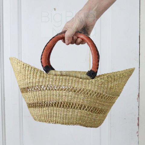 Woven handbag with red handles held by a person against a white background