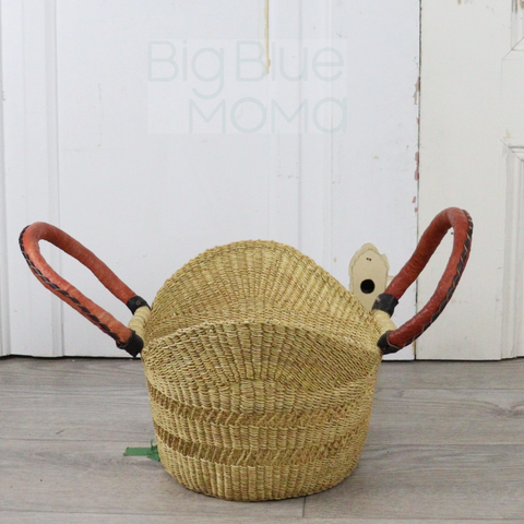 Woven basket with red handles on a wooden floor against a white paneled wall.