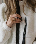 Person holding a black makeup brush with a visible brand name, wearing a white fleece jacket.