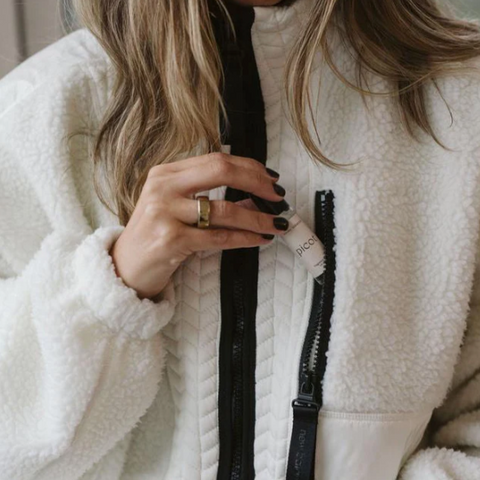 Person holding a black makeup brush with a visible brand name, wearing a white fleece jacket.
