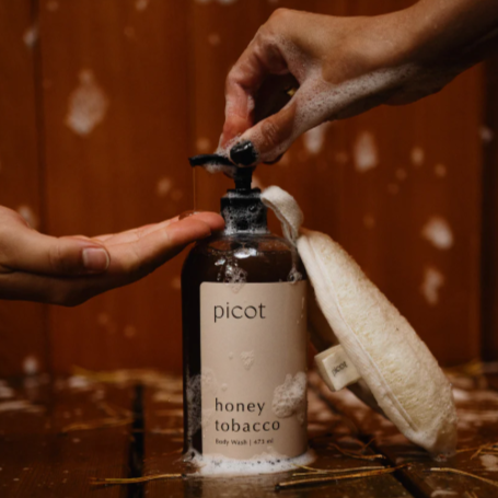 Person holding a bottle labeled 'picot honey tobacco' with a wooden background