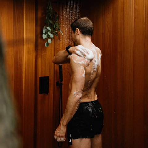 Man showering with soap lather on his back in a wooden shower stall.