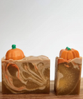 Two pumpkin-shaped soaps on a wooden block with a website interface in the background.