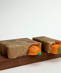 Two soap bars with pumpkin designs on a wooden board against a white background