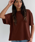 Woman wearing a brown oversized t-shirt and blue jeans against a white background