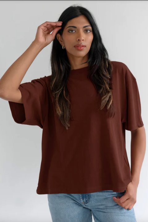 Woman wearing a brown oversized t-shirt and blue jeans against a white background