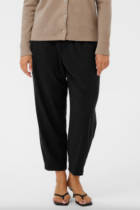 Person wearing black pants and a beige cardigan on a white background