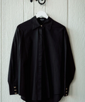 Black shirt on a hanger against a light wooden panel background