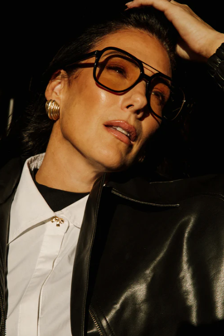 Person wearing a black leather jacket and gold earrings with a dark background