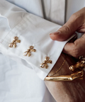 Gold brooches on a white jacket with a hand adjusting one of them.