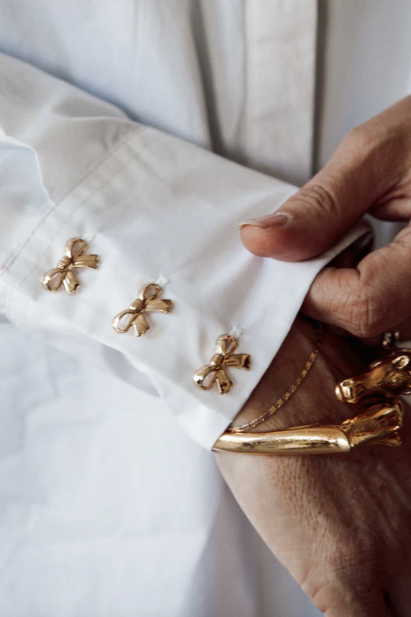 Gold brooches on a white jacket with a hand adjusting one of them.