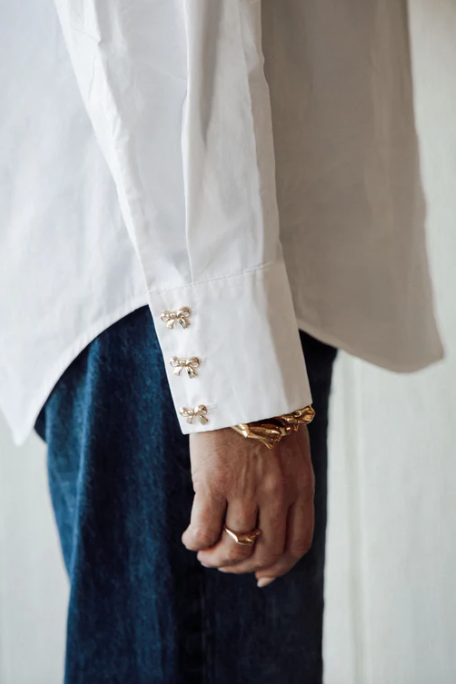 Close-up of a person wearing a white shirt with gold buttons and a beige jacket, holding a white object.