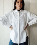 Woman wearing a white shirt and blue jeans against a light wooden panel background