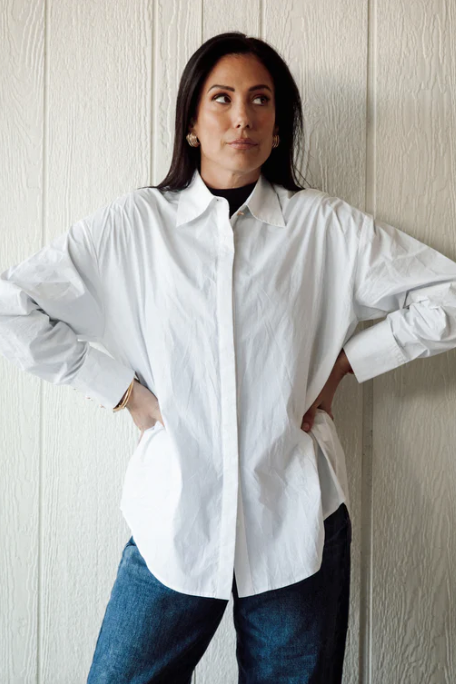 Woman wearing a white shirt and blue jeans against a light wooden panel background