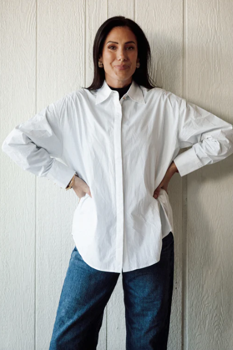 Person wearing a white shirt and blue jeans against a wooden paneled wall.