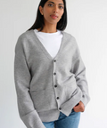 Woman wearing a gray cardigan over a white shirt with a plain background
