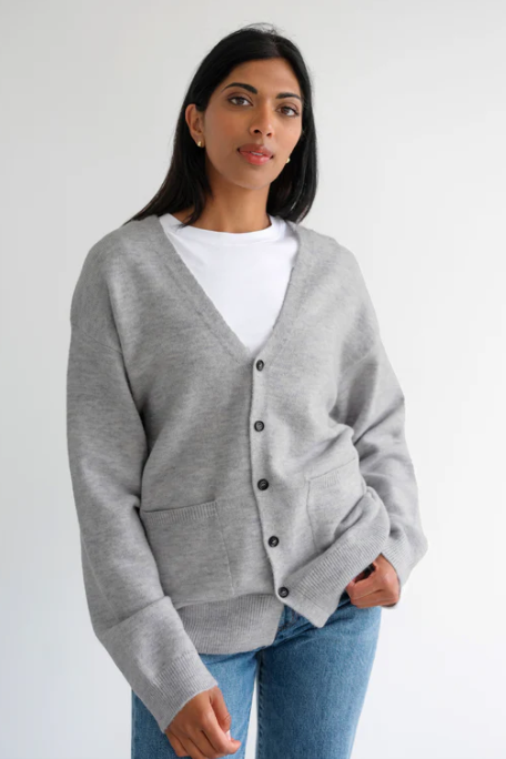 Woman wearing a gray cardigan over a white shirt with a plain background