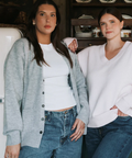 Two women standing close together in a casual setting with a shelf in the background.