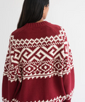 Person wearing a red sweater with white geometric patterns on a plain background