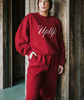 Person wearing a red 'Uplift' sweatshirt and pants against a wooden wall.