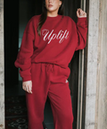 Person wearing a red 'Uplift' sweatshirt and pants standing in a doorway.