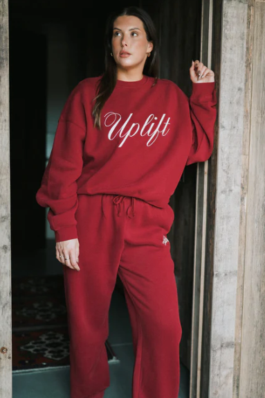 Person wearing a red 'Uplift' sweatshirt and pants standing in a doorway.