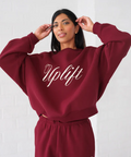 Person wearing a burgundy 'Uplift' sweatshirt and pants on a white background