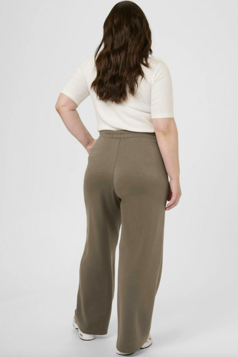 Woman wearing a white top and brown pants on a gray background