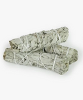 Two bundles of sage smudge sticks tied with twine on a white background