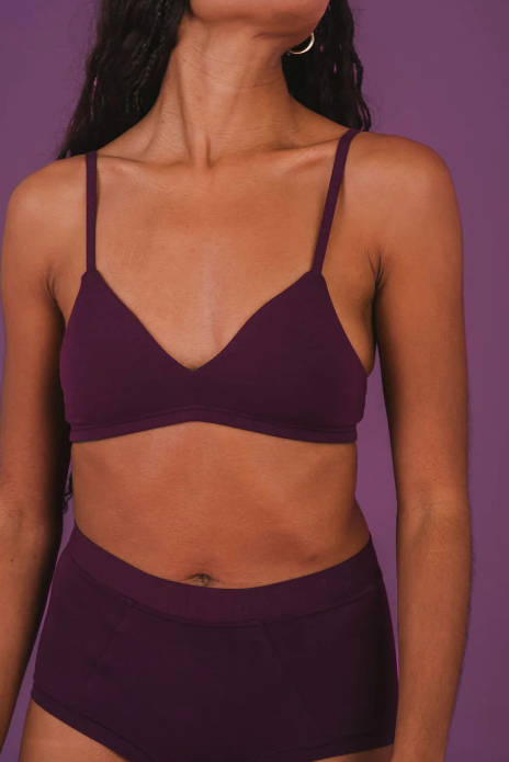 Person wearing a purple sports bra and shorts against a purple background