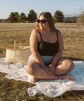 Woman sitting on a white blanket in a field with a woven basket beside her.
