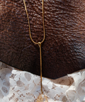 Gold necklace draped over a brown leather surface with lace fabric underneath