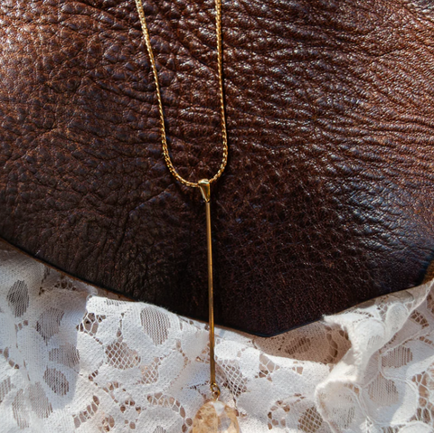 Gold necklace draped over a brown leather surface with lace fabric underneath