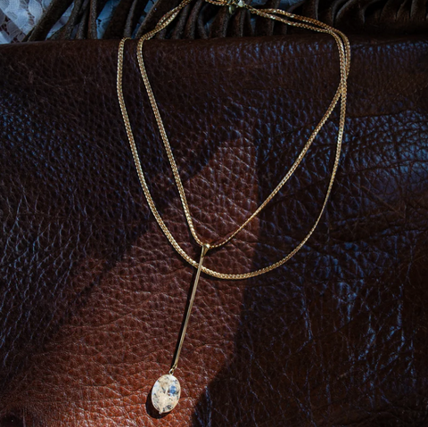 Gold necklace with a pendant on a brown leather surface