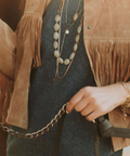 Person wearing a fringe jacket with jewelry, holding a chain.