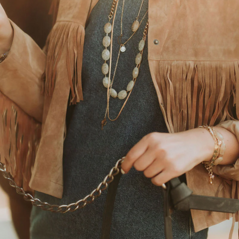 Person wearing a fringe jacket with jewelry, holding a chain.