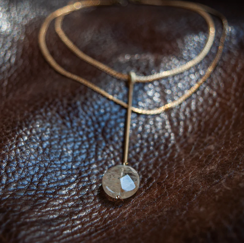 Gold necklace with a pendant on a brown leather surface