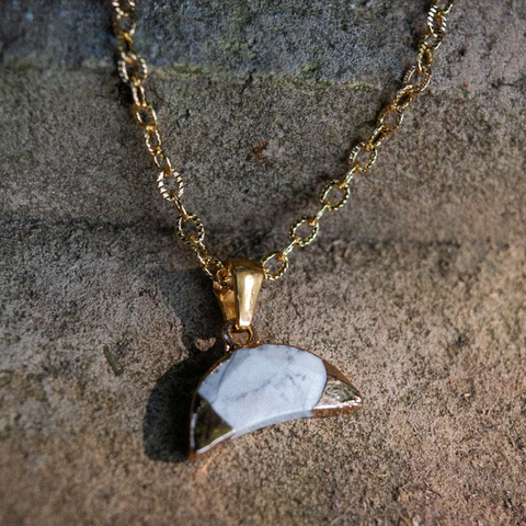 Gold necklace with a triangular pendant on a textured stone background
