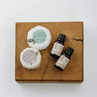 Two soap bars and two small bottles on a wooden block with a white background