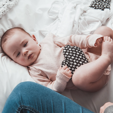 Baby lying on a white blanket with a person holding the baby's hand