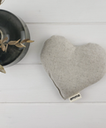 Heart-shaped gray pillow with a plant on a white wooden surface
