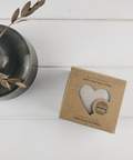 Kraft paper box with heart design on a white wooden surface next to a vase with leaves.