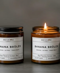 Two 'Isle of Rose Banana Brèlé' candles on a gray background, one lit.