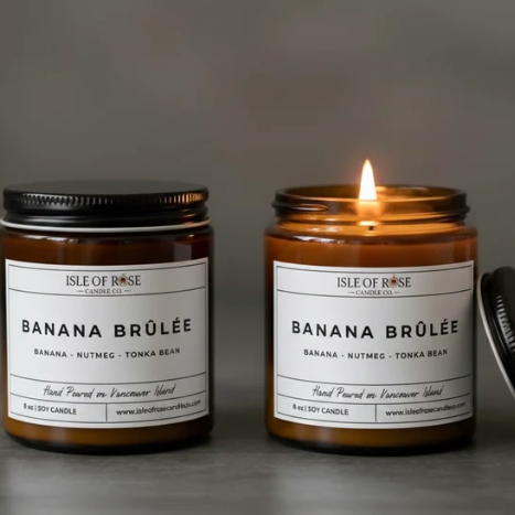 Two 'Isle of Rose Banana Brèlé' candles on a gray background, one lit.