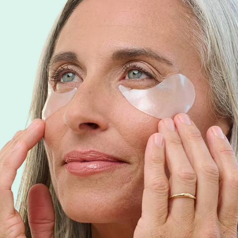 Woman applying eye patches with a teal background