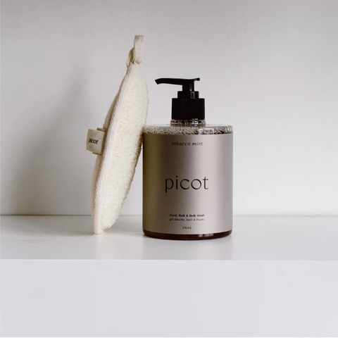 Picot body wash bottle with a pump and washcloth on a white surface