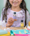 Child holding a bottle labeled 'naturals' with various other bottles and items on a table.